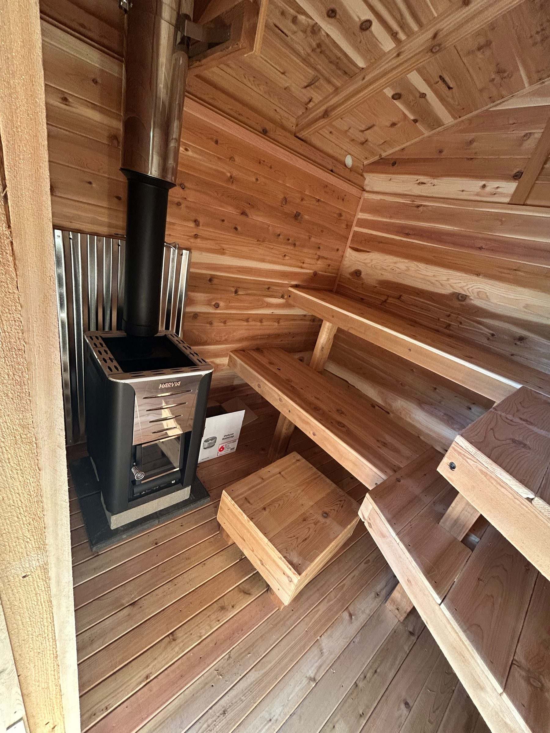 Harvia wood-burning sauna stove with a stainless heat shield inside a cedar sauna with tiered benches