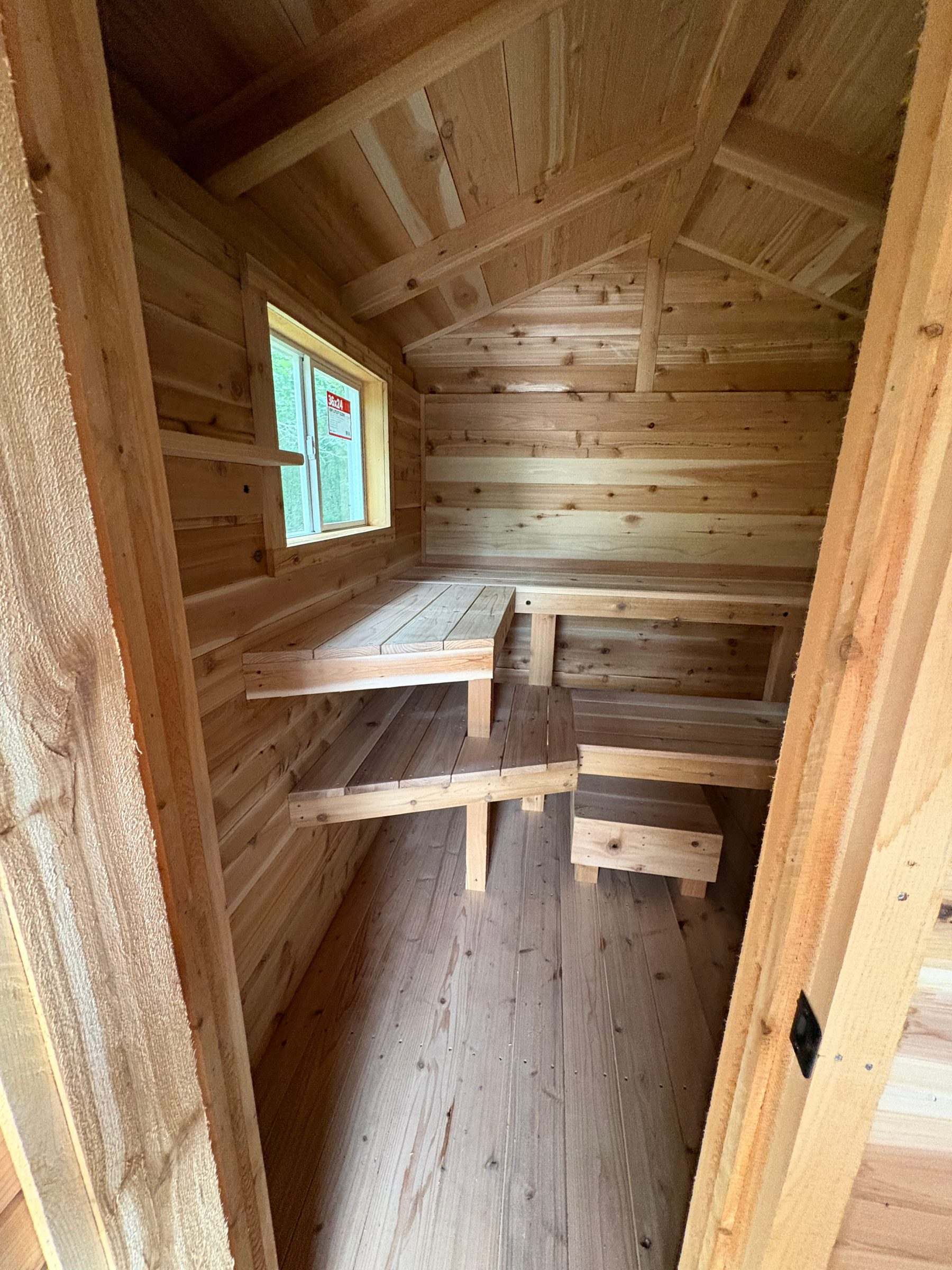 Hot room of a cedar sauna with tiered L-shaped benches, a foot stool and a window
