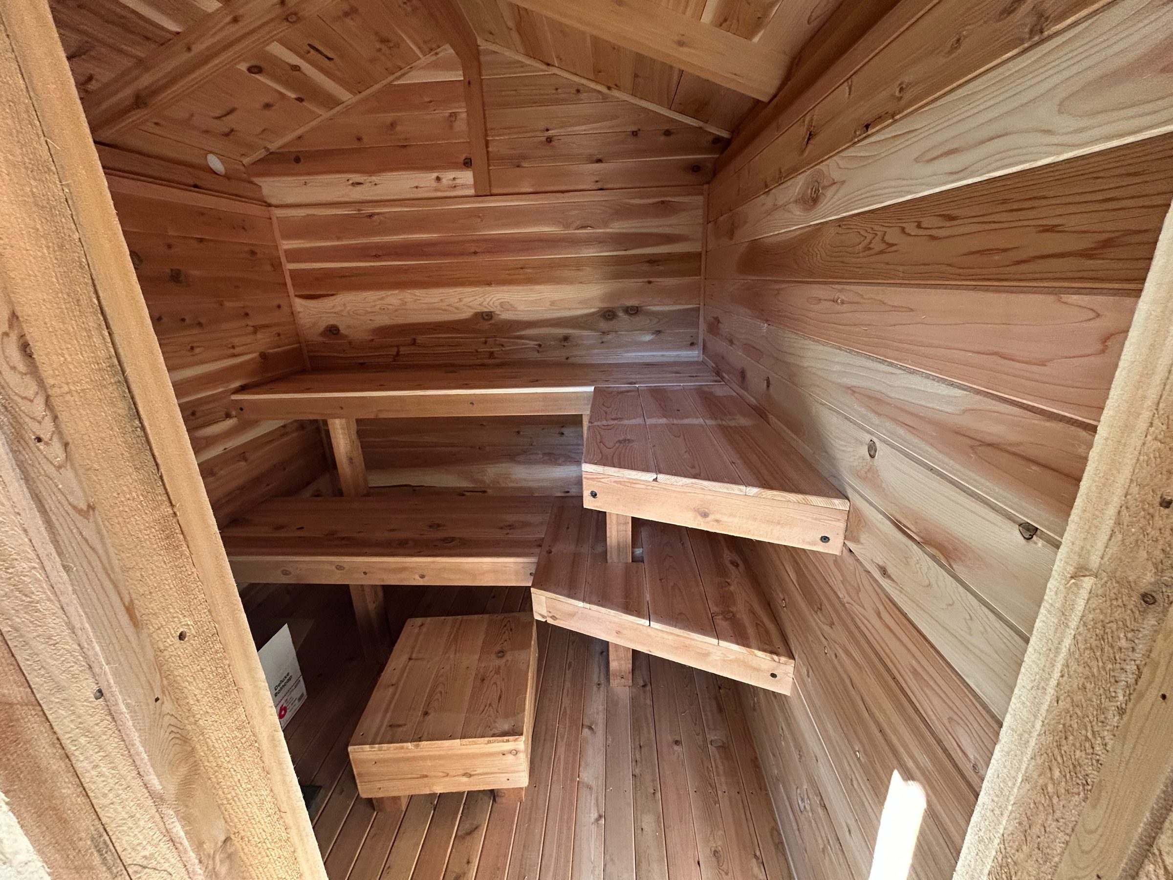 Interior of a cedar sauna with tiered L-shaped benches, a foot stool and a vaulted cedar ceiling
