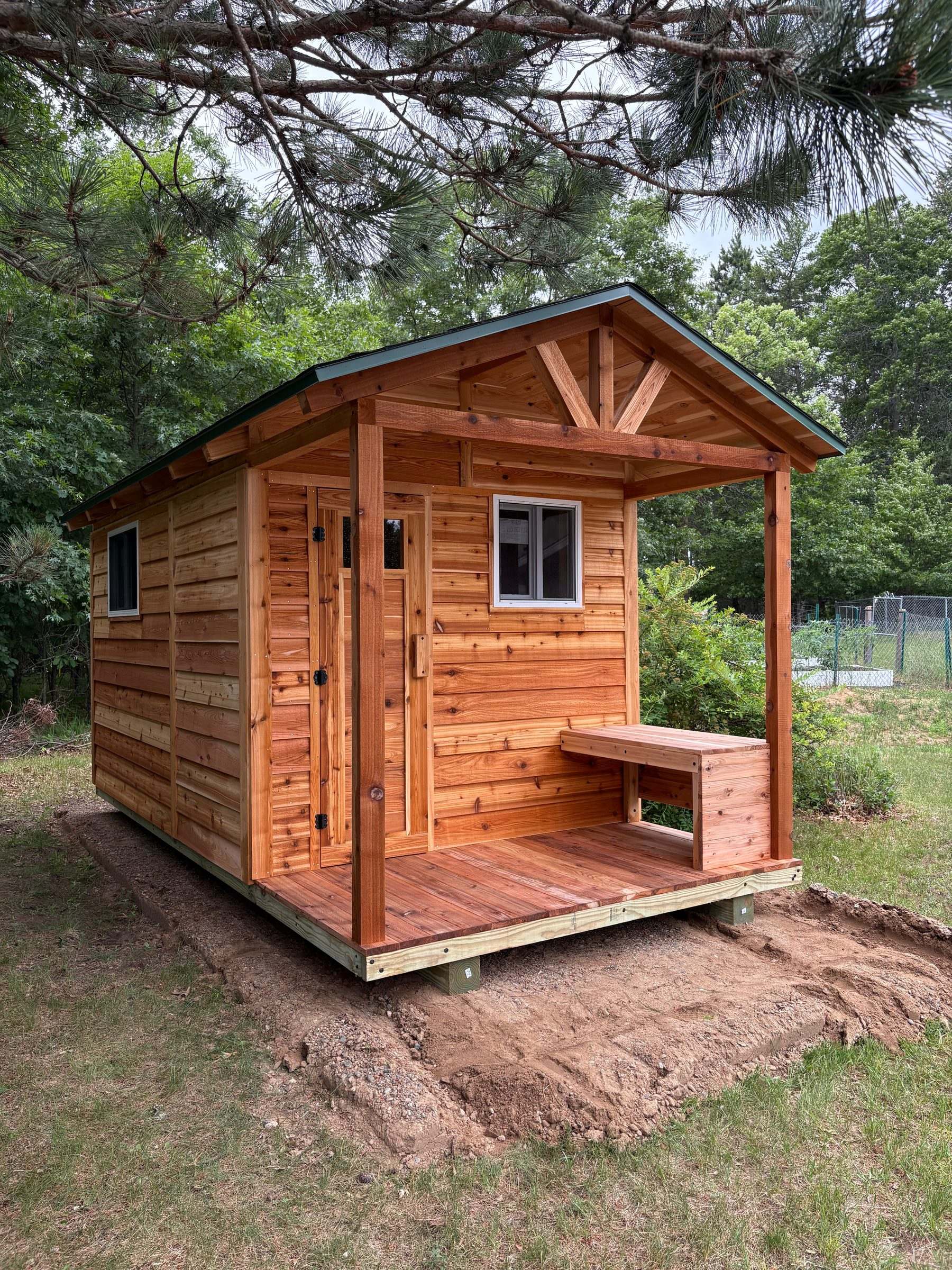 Cedar outdoor sauna with a changing room, a covered porch with a bench and a green metal roof