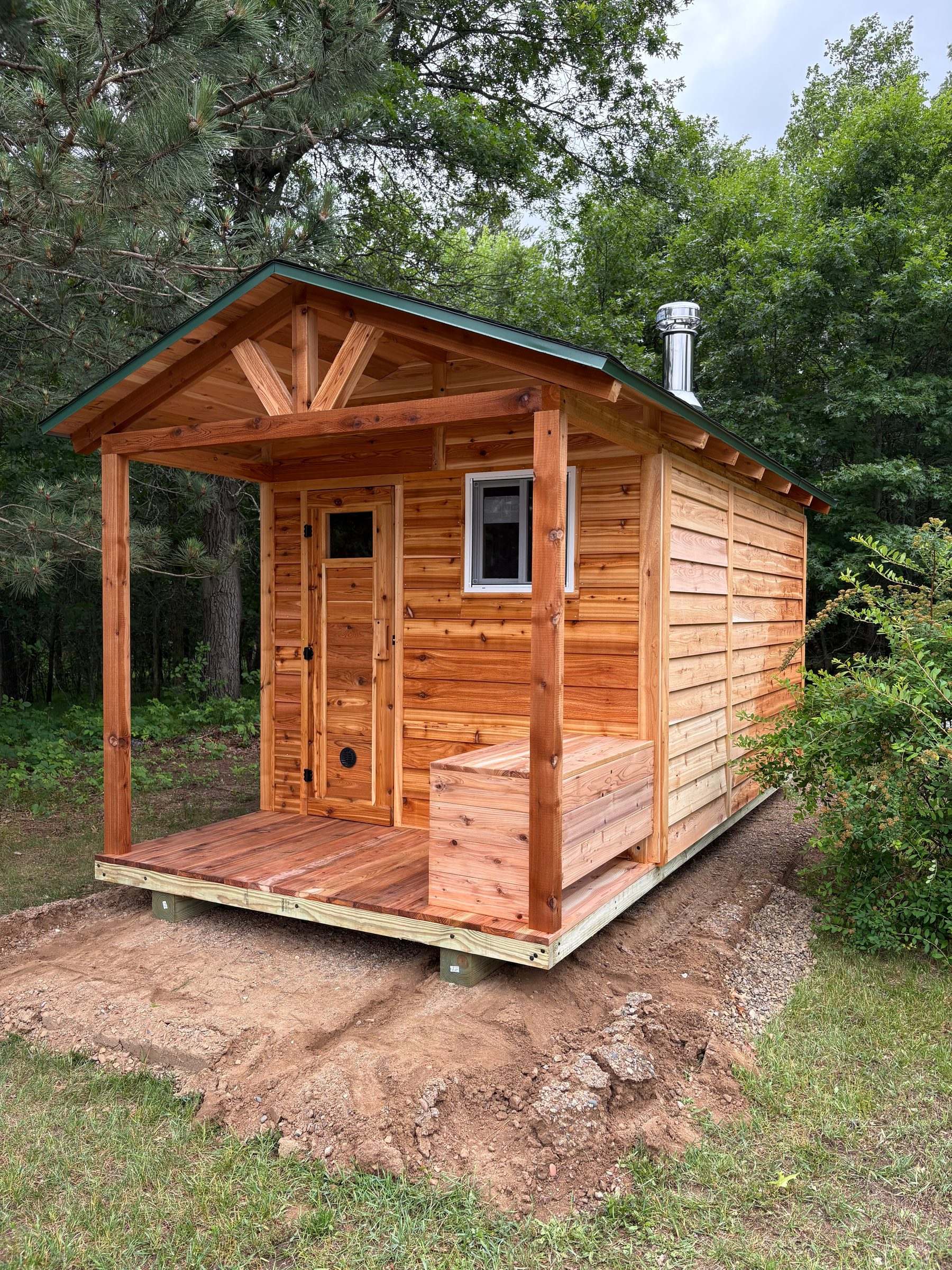 Cedar outdoor sauna with a changing room, covered porch, bench and stainless chimney