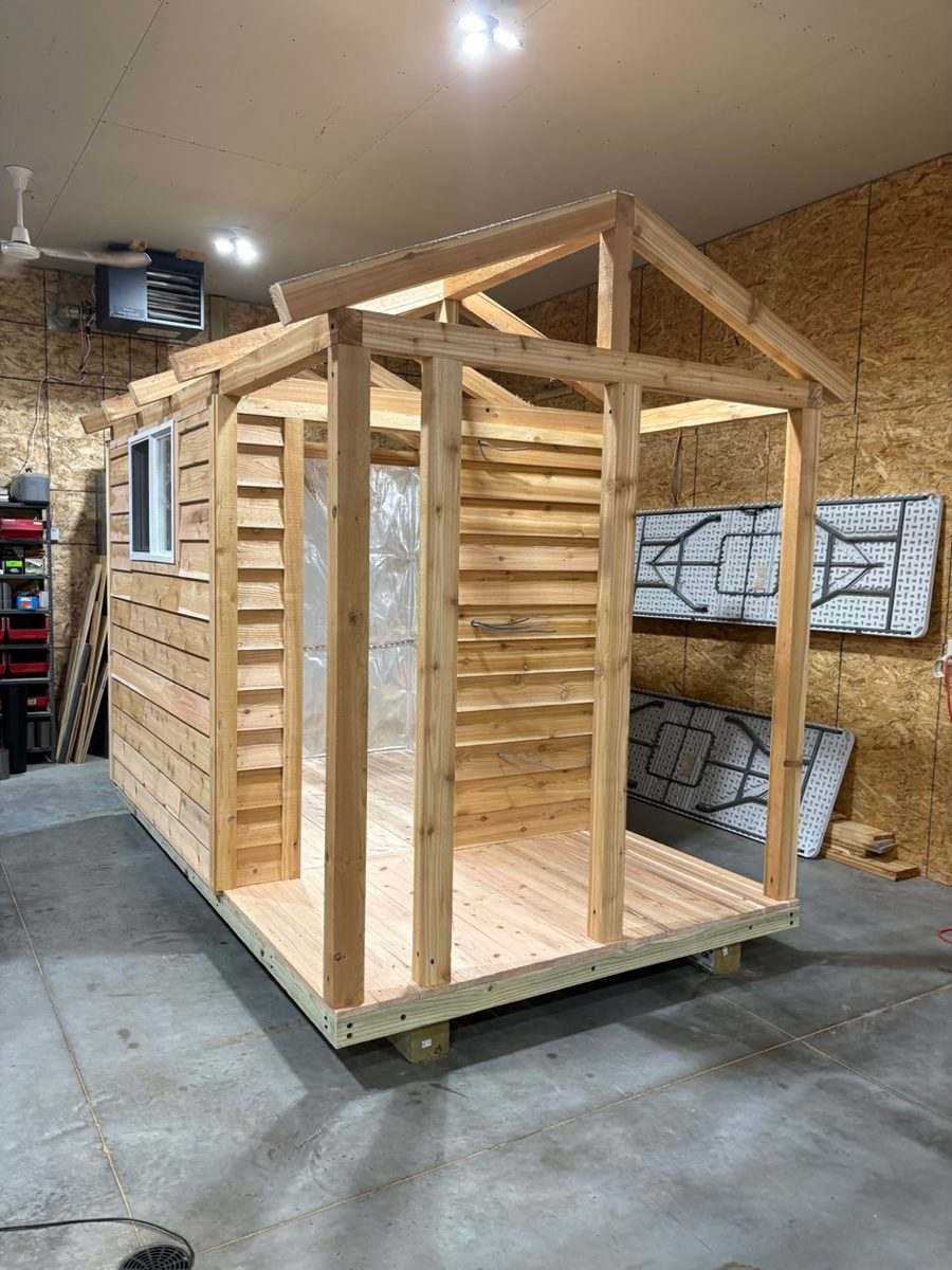 Custom cedar sauna under construction inside a workshop, with porch posts and roof rafters