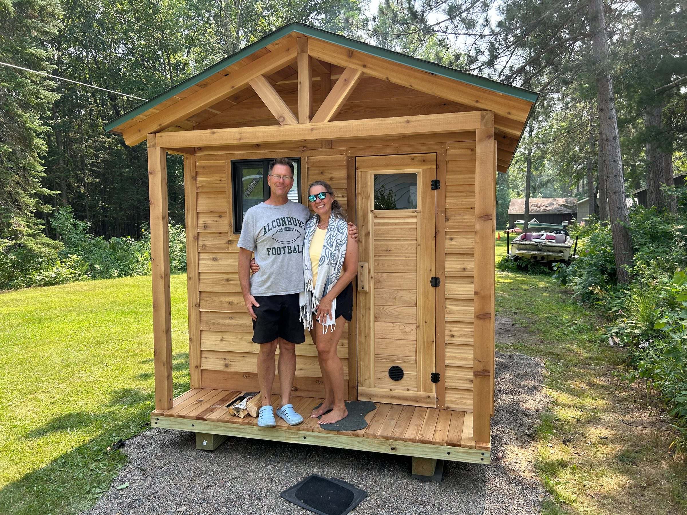 Two smiling customers standing on the front porch of their new cedar sauna
