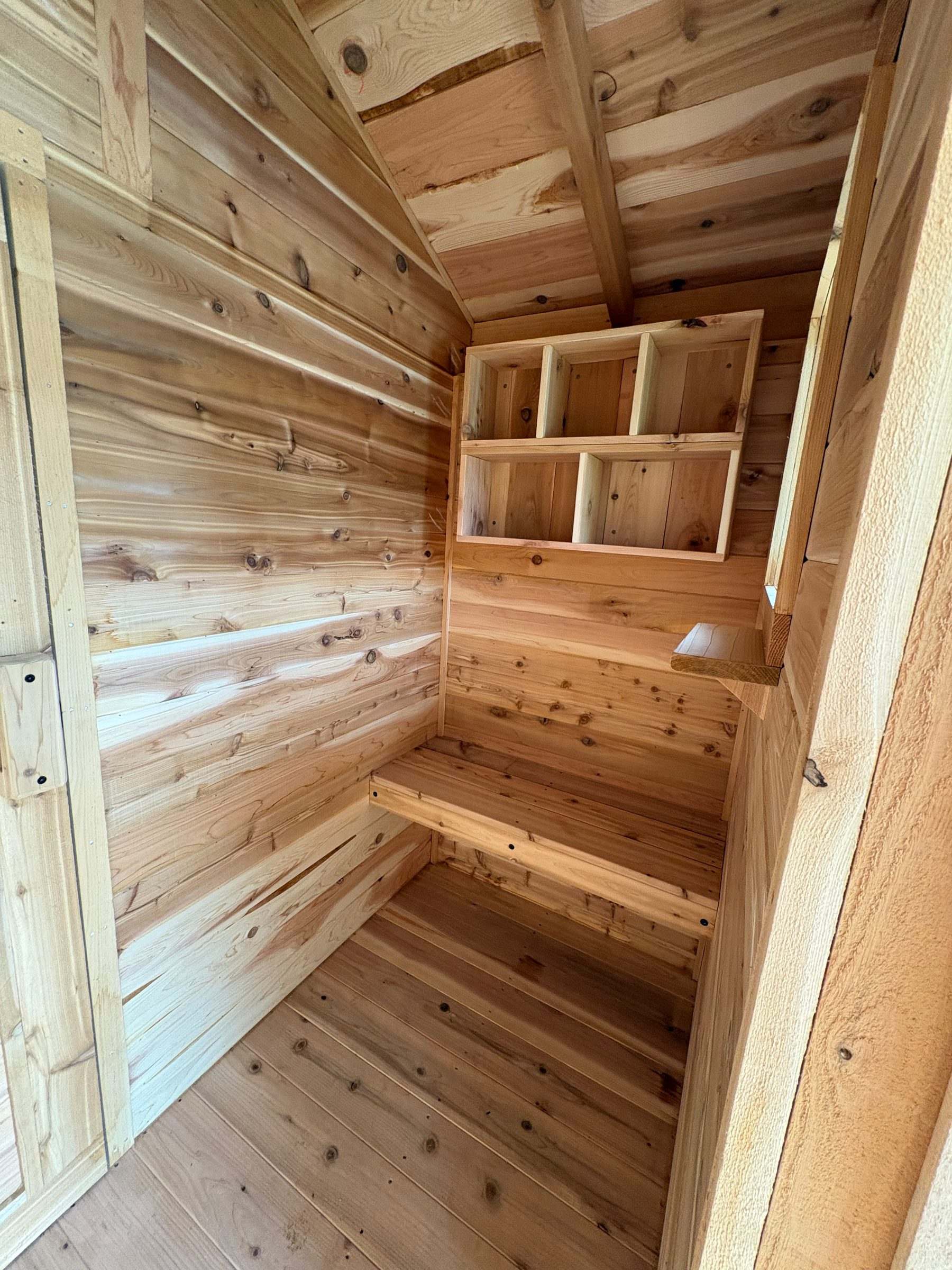 Cedar sauna changing room with built-in cubby shelves, a bench and a small shelf