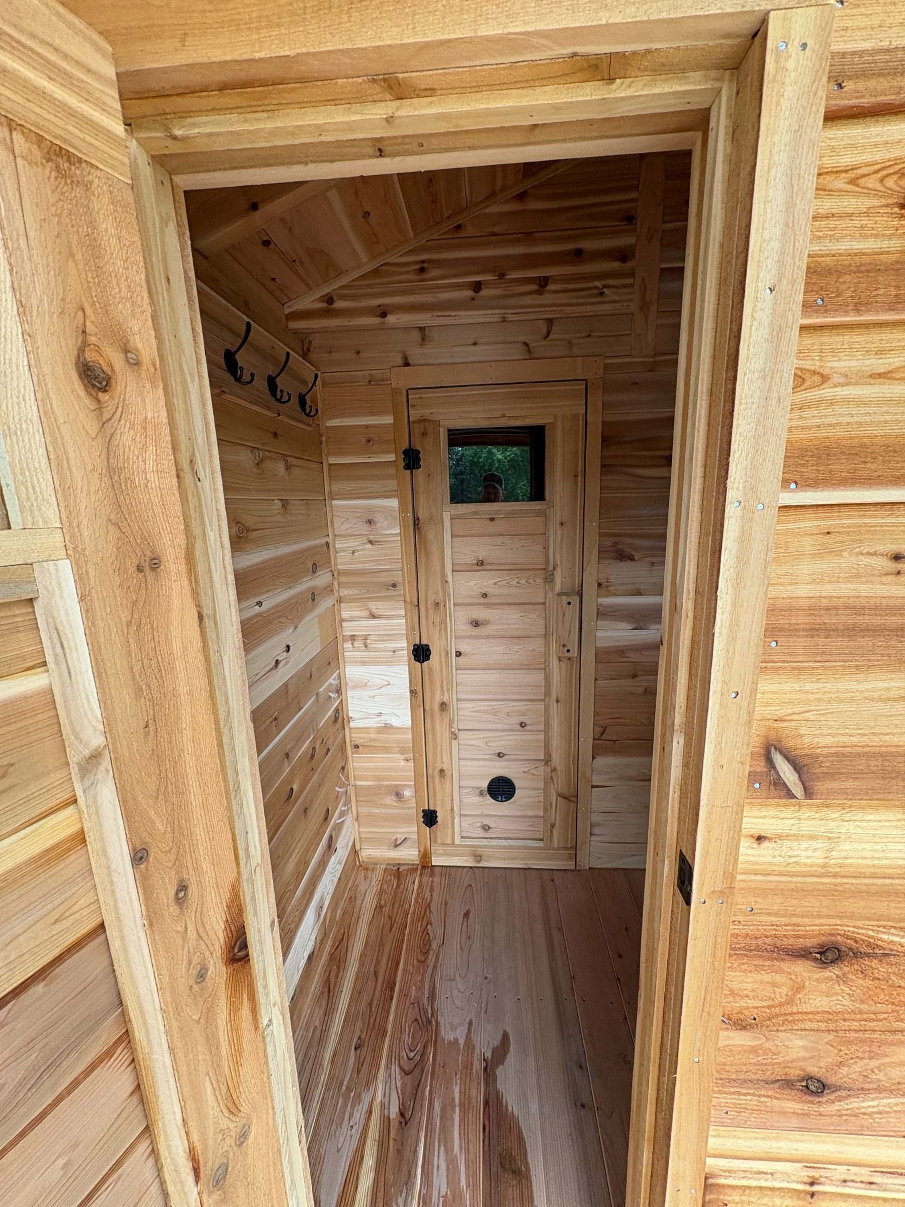 View through the entry into a cedar changing room with towel hooks, leading to the glass-window door of the hot room