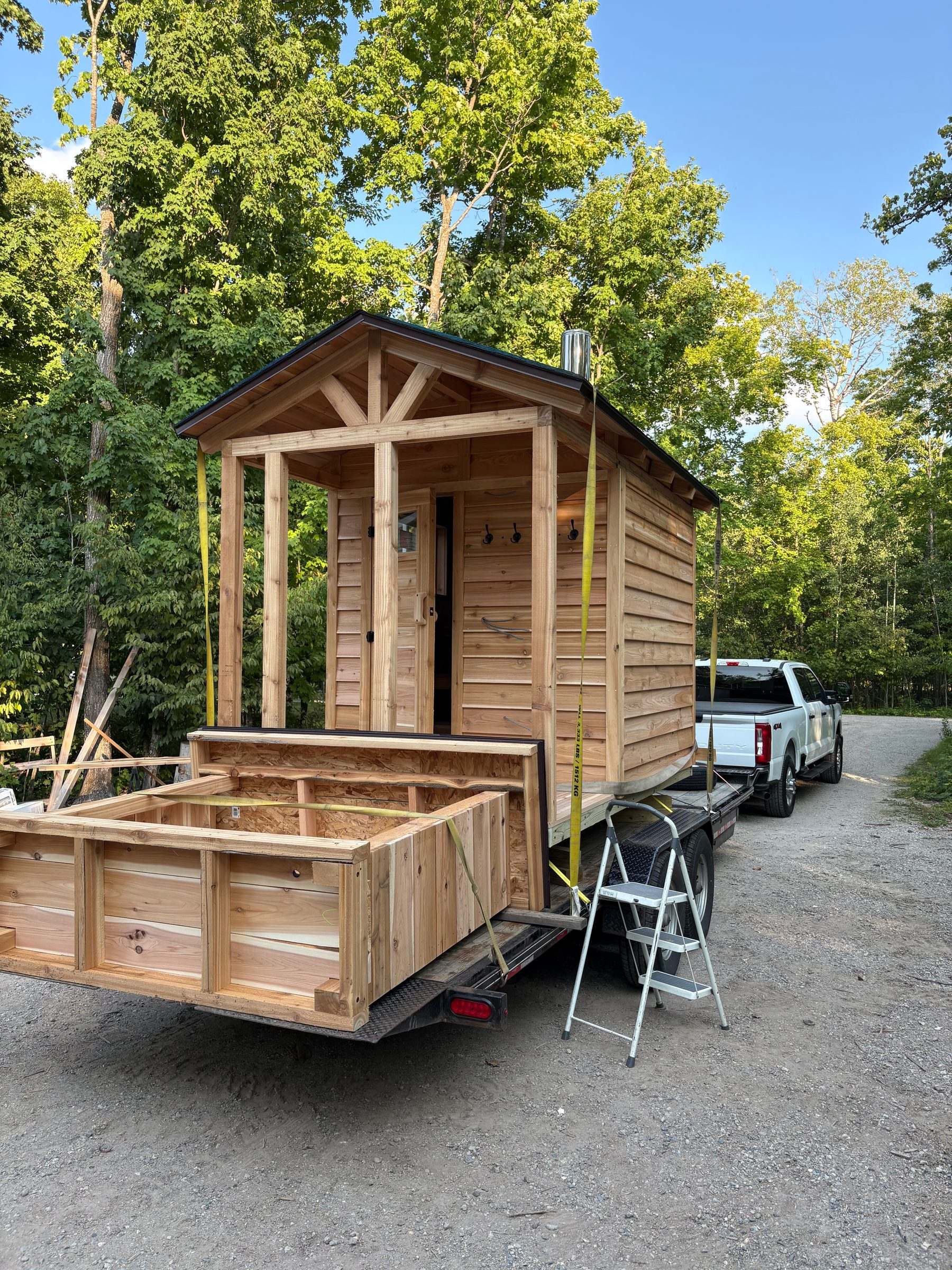 Fully assembled cedar sauna and matching woodshed strapped to a trailer, ready for delivery