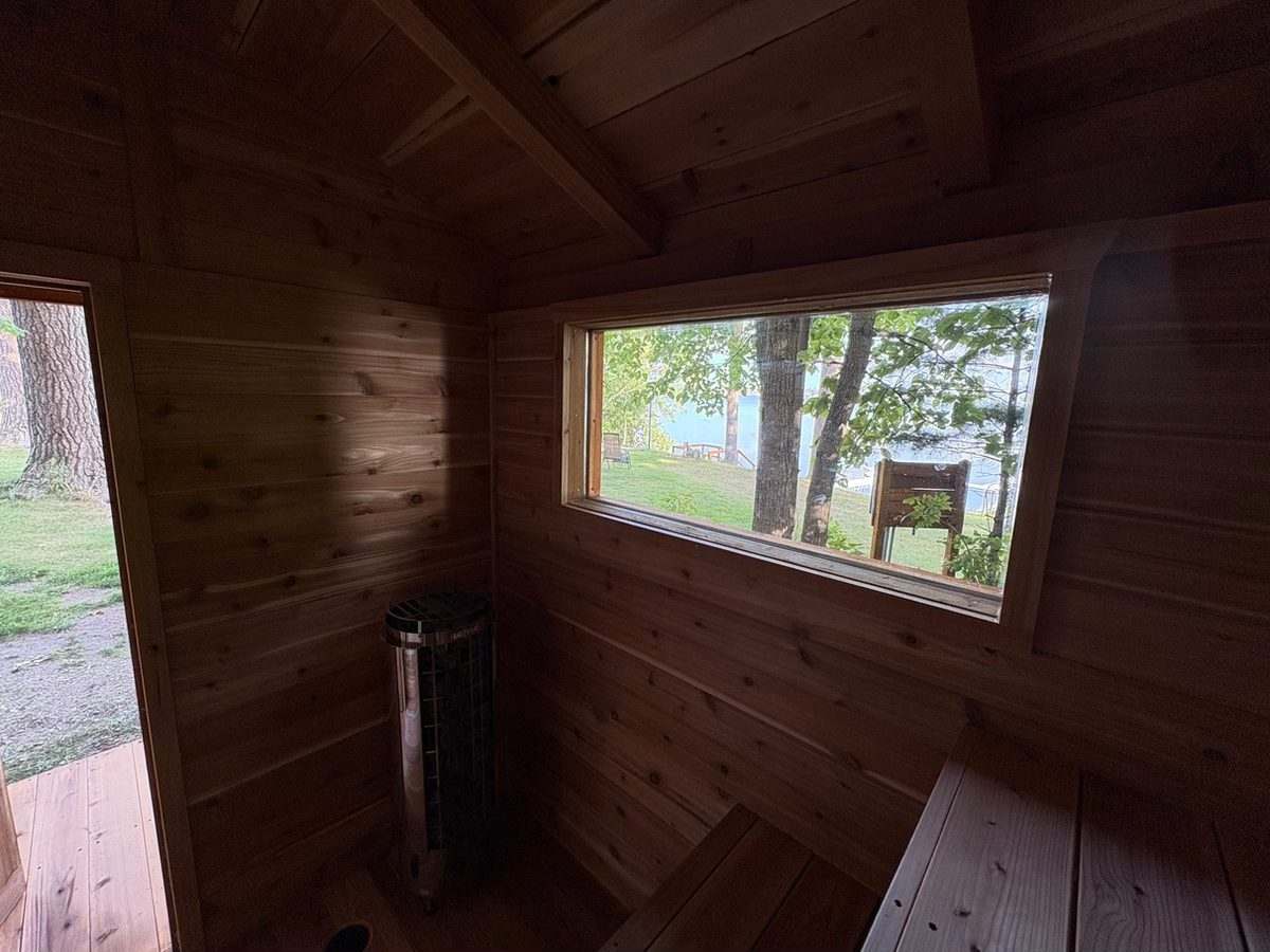 Cedar sauna interior with an electric heater and a wide window looking out to the lake