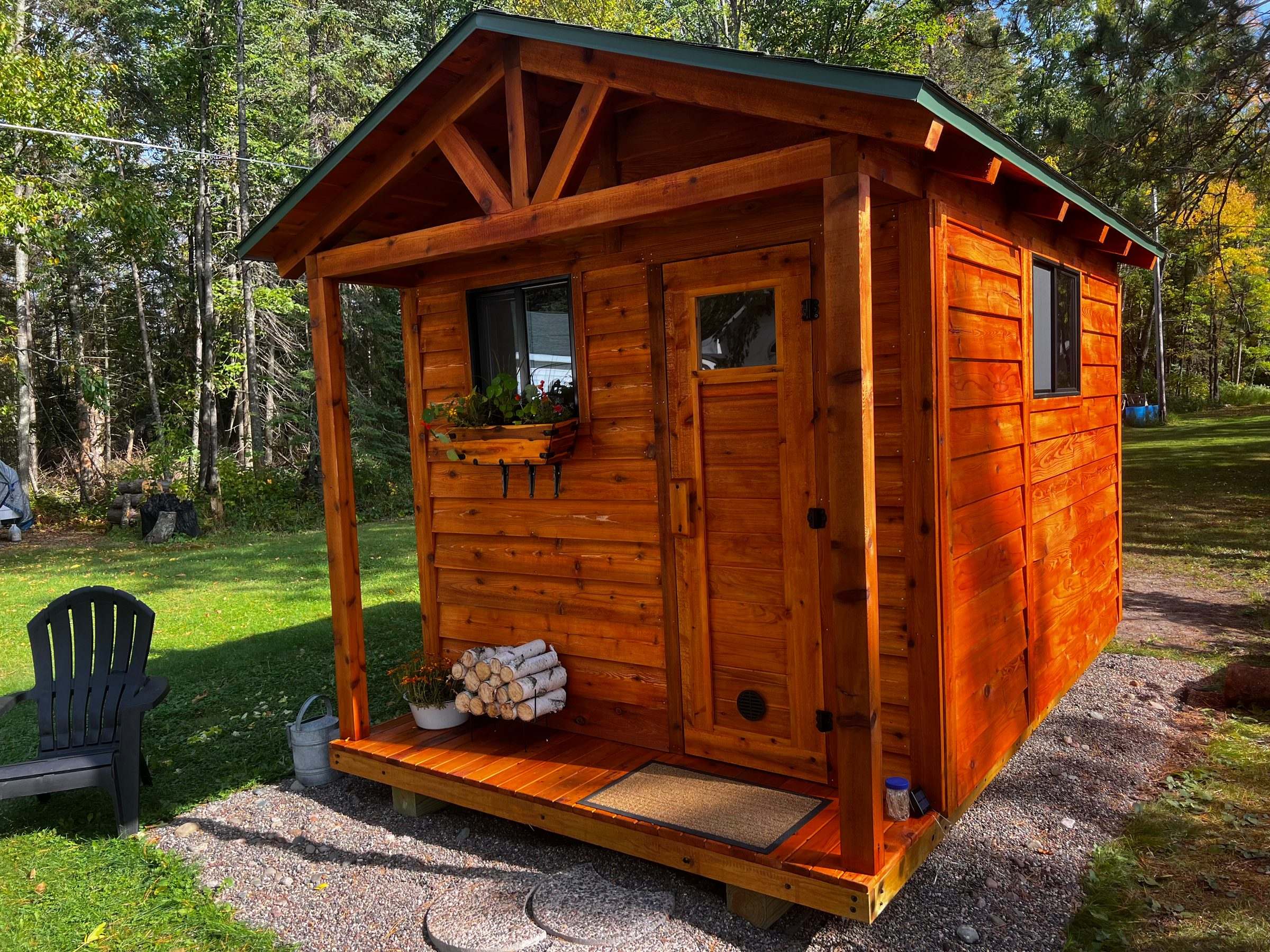 Stained cedar outdoor sauna with a green metal roof, front porch and window flower box