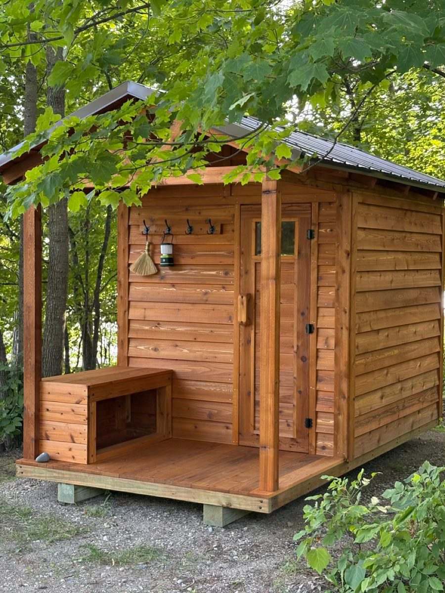 Covered sauna porch with a cedar storage bench, towel hooks, a lantern and a sauna whisk