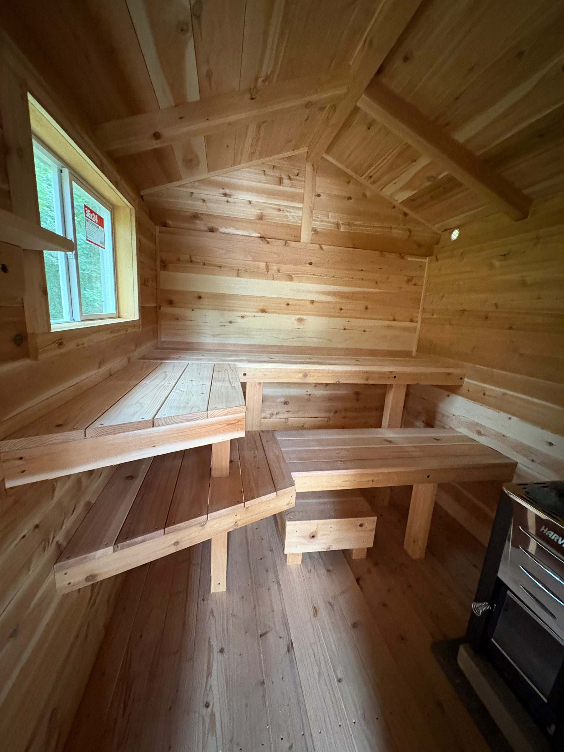 Wood-fired cedar sauna interior with tiered benches, a window and a Harvia stove